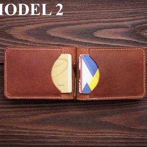 May include: A brown leather wallet with a money clip and two card slots. The wallet is open and has two cards inside. The text "MODEL 2" is visible at the top of the image.