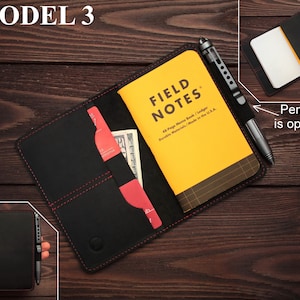 Puede incluir: Cartera de cuero negro para cuaderno con costuras rojas, un cuaderno Field Notes amarillo y un bol&iacute;grafo plateado. La cartera tiene un bolsillo para tarjetas y efectivo. "Penslip is optional" est&aacute; escrito en la imagen.