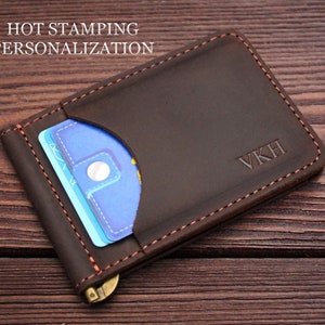 May include: Brown leather wallet with a money clip and a card slot. The wallet has a personalised inscription that reads "VKH".