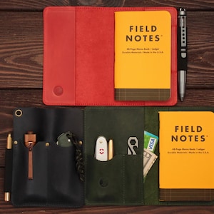 Puede incluir: Dos cubiertas de cuero para cuaderno, una roja y otra verde, con cuadernos Field Notes en su interior. La cubierta verde tiene varios bolsillos y un bol&iacute;grafo, una navaja peque&ntilde;a y una multiherramienta en su interior.