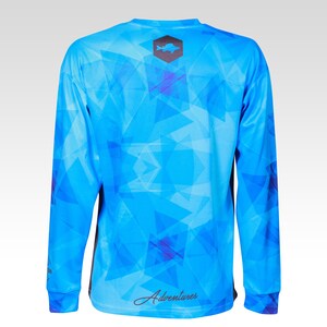 May include: A blue long-sleeve shirt with a geometric pattern and a black fish logo on the back. The shirt also has the word "Adventures" written on the back.
