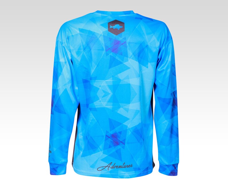 May include: A blue long-sleeve shirt with a geometric pattern and a black fish logo on the back. The shirt also has the word "Adventures" written on the back.