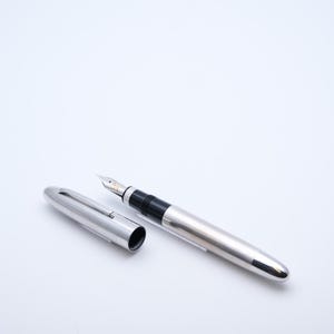 May include: A silver fountain pen with a black grip and a silver cap. The cap is lying next to the pen. The pen has a silver body and a silver nib. The pen is on a white background.