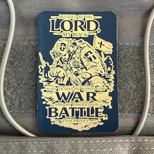 Könnte beinhalten: Ein rechteckiger, marineblauer Aufnäher mit goldfarbenem Text und Illustrationen. Er zeigt einen Soldaten mit Waffe, eine Flagge mit Kreuz und den Text "BLESSED BE THE LORD MY ROCK" und "WHO TRAINS MY HANDS FOR WAR AND MY FINGERS FOR BATTLE. PSALM 144:1."