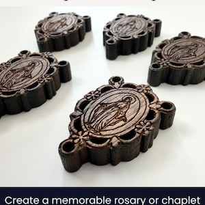 May include: Wooden rosary centerpieces with a detailed engraving of a religious figure. The dark brown pieces are oval-shaped with decorative edges and a hole for stringing. The image also includes the text "Miraculous Medal Rosary & Chaplet Centerpiece".