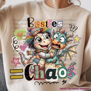 Puede incluir: Sudadera beige con un gráfico colorido de dos dragones de dibujos animados abrazándose. El texto "Besties Chaos" se muestra arriba y abajo de los dragones, con elementos decorativos como corazones y estrellas.