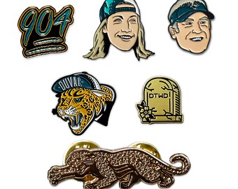Può includere: Set di sei spille smaltate con una varietà di design, tra cui un giaguaro, una lapide con il testo "DTWD", una persona con un berretto da baseball turchese e il numero "904".