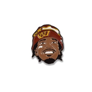 Könnte beinhalten: Anstecknadel mit einem lächelnden Cartoon-Gesicht mit braunem Teint, das einen bordeauxroten und goldenen Hut trägt. Der Hut hat den Buchstaben "W" darauf. Die Anstecknadel ist vor einem weißen Hintergrund platziert.