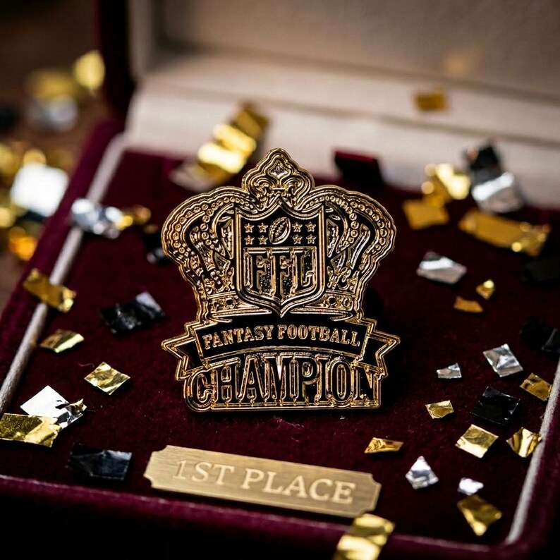 Op de afbeelding: Een goudkleurige Fantasy Football Champion-speld met een kroonontwerp, geplaatst in een bordeauxrode fluwelen doos. De speld toont het NFL-logo en de woorden "Fantasy Football Champion". Een klein plaatje leest "1st Place".