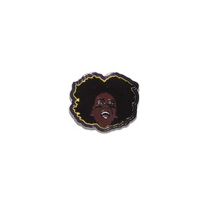 May include: A black and brown enamel pin featuring a portrait of a person with an afro hairstyle. The person is smiling with their mouth open and their eyes are closed. The pin has a purple and yellow outline.