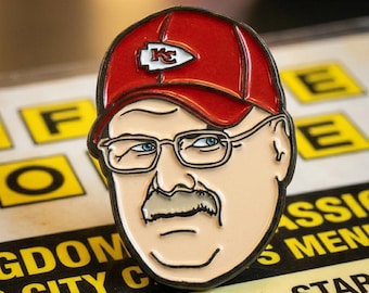 Puede incluir: Un pin que presenta una imagen de dibujos animados de un hombre que lleva una gorra de béisbol roja con un logotipo blanco y rojo. El hombre tiene gafas, bigote y ojos azules. El pin está sobre un menú con texto amarillo y negro.