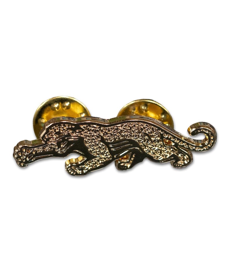 May include: Gold-colored metal pin featuring a detailed design of a running jaguar. The pin has a back post for attaching to clothing or a bag.