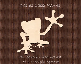 May include: A laser cut wooden frog cutout, made from 1/4 inch maple plywood. The frog is in a sitting position with one arm raised. The text "Dallas Laser Works" is at the top of the image and the text "All items are laser cut out of 1/4" Maple Plywood" is at the bottom of the image.