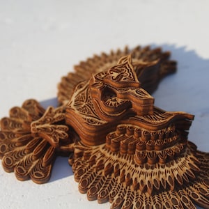May include: A wooden owl sculpture with intricate details and layered wings. The owl is carved from light brown wood and has a detailed design.