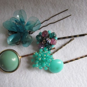 May include: Assortment of hair clips featuring turquoise and purple beads, a turquoise flower, and a turquoise round bead. The hair clips are gold colored.