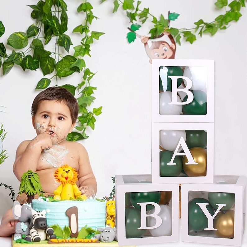 Puede incluir: Cuatro cajas blancas con lados transparentes apiladas una encima de la otra. Cada caja contiene globos verdes y blancos y una letra blanca que deletrea la palabra "BABY".