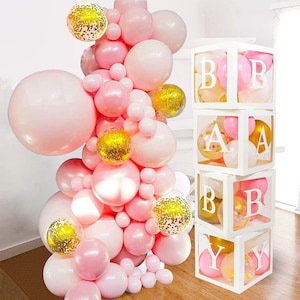 Puede incluir: Una caja blanca con las letras "BABY" escritas en cajas individuales. Las cajas est&aacute;n llenas de globos rosas y blancos. Las cajas est&aacute;n rodeadas de una gran disposici&oacute;n de globos rosas y blancos con globos de confeti dorados.