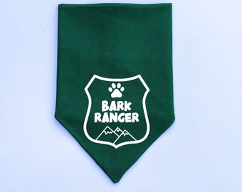 Puede incluir: Bandana verde con una huella de pata blanca y el texto "Bark Ranger" dentro de un escudo blanco con montañas en la parte inferior.