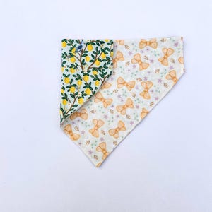 May include: A reversible dog bandana featuring a lemon tree design on one side and a yellow bow pattern on the other.