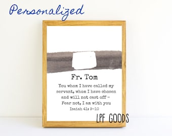 May include: A framed print with a light wood frame. The print features the name "Fr. Tom" above a quote from Isaiah 41:9-10. The words "Personalized" and "LPF GOODS" are also visible.