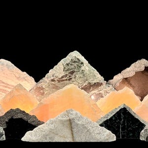 May include: A collection of various crystals and minerals arranged in a mountain-like formation against a black background. The crystals display a range of colors, including white, orange, black, and green, with varying textures and shapes.