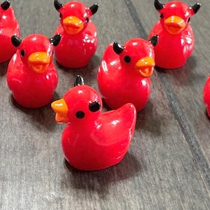 May include: A collection of ten red devil-themed figurines with black horns and orange beaks. The figurines are made of a glossy material and have a cartoonish appearance.