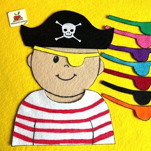 May include: A felt pirate character with a black hat featuring a skull and crossbones, a yellow eye patch, and a red and white striped shirt. Includes several colorful eye patches in green, pink, purple, blue, red, black, and orange.