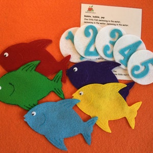May include: A felt educational set with colorful fish and numbered circles. The fish are red, green, blue, yellow, and purple. The circles are white with blue numbers 1-5. A card with the text "Bubble, bubble, pop" is also included.