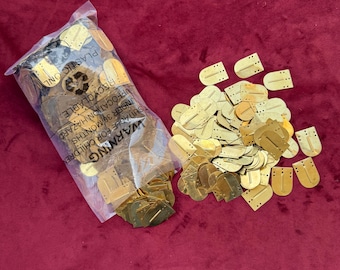 May include: A collection of small, gold-colored metal U-shaped fasteners with two small holes at the top and a central vertical slit. Some fasteners are loose in a pile, while others are contained within a clear plastic bag with warning text.