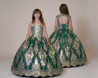May include: A floor-length emerald green dress featuring a gold sequin damask pattern. The bodice has a scoop neckline and the back includes a keyhole cutout with a lace-up corset closure and a matching green ribbon tie at the waist.