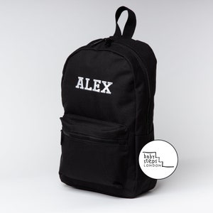 May include: Black canvas backpack with a white embroidered name "ALEX" and a white logo on the side that says "baby steps LONDON".