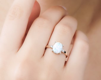 Puede incluir: Un anillo de oro con una piedra de ópalo blanco y dos piedras transparentes más pequeñas en la banda.