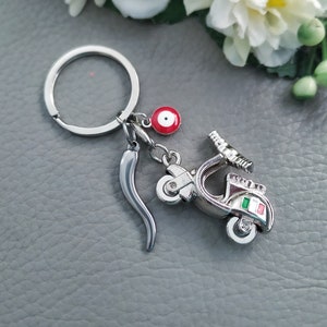 May include: Silver keychain with a red and white evil eye charm, a silver chili pepper charm, and a silver scooter charm with an Italian flag on the side.