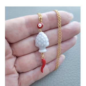 May include: A gold chain necklace with a white ceramic artichoke charm, a red chili pepper charm, and a red and blue evil eye charm.
