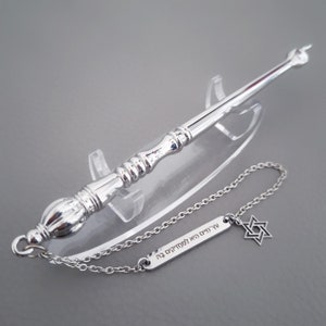 May include: A silver yad with a chain and a Star of David charm. The charm has the Hebrew text "עץ חיים היא למוצאי" engraved on it.