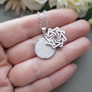 May include: Silver necklace with a round pendant featuring a circular design with Georgian text and a smaller pendant with a geometric design.