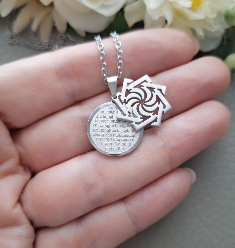 May include: Silver necklace with a round pendant featuring a circular design with Georgian text and a smaller pendant with a geometric design.