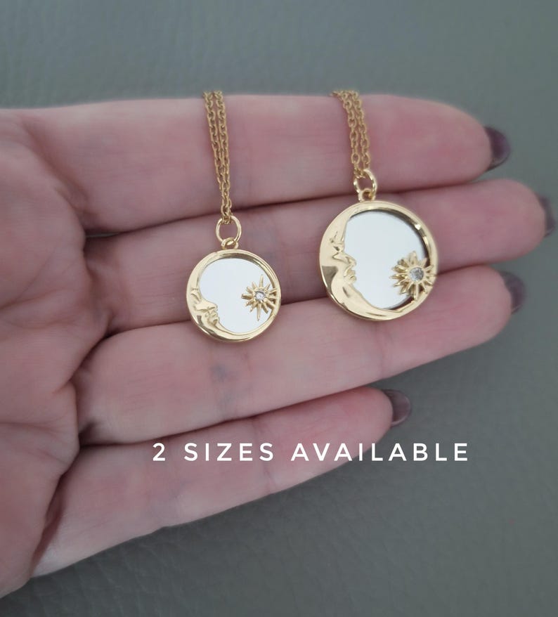 May include: Two gold-toned circular pendant necklaces featuring a crescent moon and a sun motif with a small embedded stone. The pendants have a reflective centre and are suspended from thin gold chains. The text 2 SIZES AVAILABLE is visible.