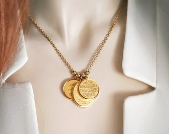 May include: A gold-toned necklace featuring a delicate chain and three circular pendants. Each pendant is engraved with intricate Arabic calligraphy. The necklace is displayed against a white collared garment, highlighting the metallic finish.