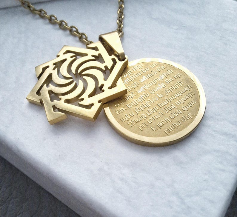 May include: Gold necklace with a pendant featuring a geometric design and a round disc with Armenian text. The text reads: "այրներ րկինս ես un լիցի անուն Քո։ Նեսցէ արքայութիւն ո։ Եղիցին կամք Քի որ պէս յերկինս և յերկրի։ Զհաց մեր հանապազո րդ տուր մեզ այսօր: և թող մեզ զպ արտիս մեր,"