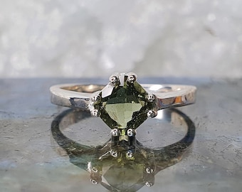Op de afbeelding: Een zilveren ring met een groene edelsteen in een zetting met zes griffen.