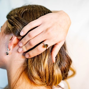 May include: A woman wearing a silver necklace and a ring with a green gemstone. The ring is on her right hand, and she is holding her hair with her left hand.