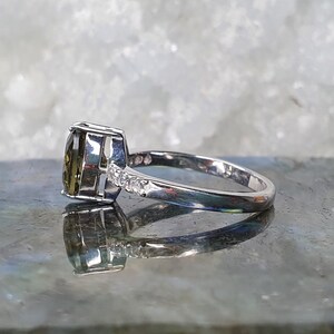 May include: A silver ring with a large, oval-shaped green gemstone and smaller clear gemstones on the band.