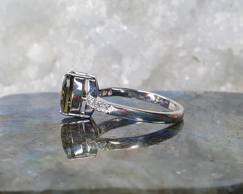 May include: A silver ring with a large, oval-shaped green gemstone and smaller clear gemstones on the band.