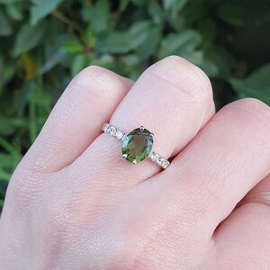 May include: A silver ring with a green oval gemstone and a band of small clear stones.