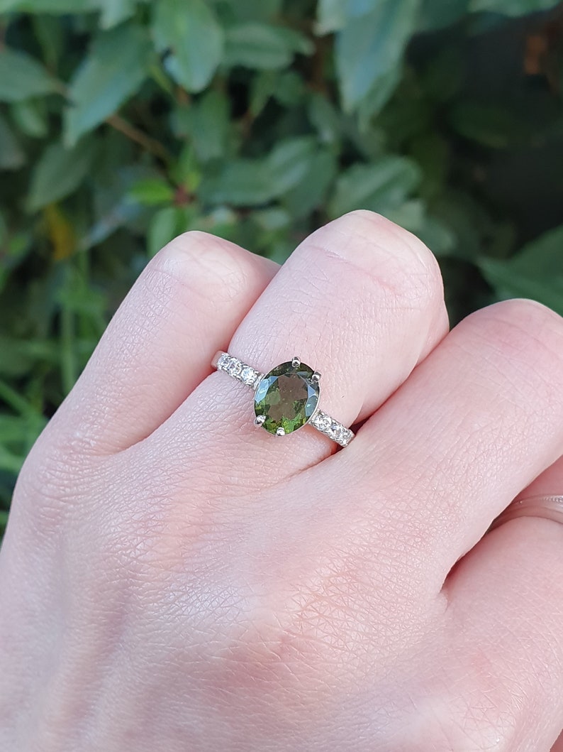 May include: A silver ring with a green oval gemstone and a band of small clear stones.