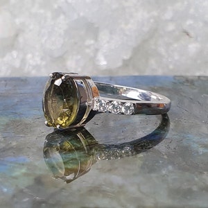 May include: A silver ring with a large, oval-shaped green gemstone and a band of small, clear gemstones.
