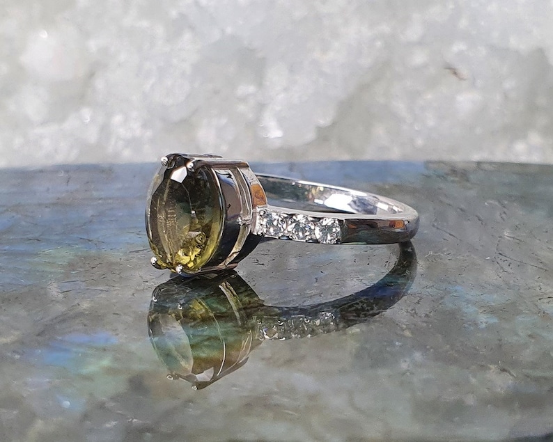 May include: A silver ring with a large, oval-shaped green gemstone and a band of small, clear gemstones.