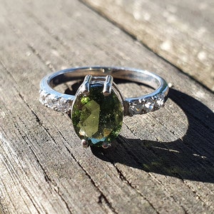 May include: A silver ring with a green oval gemstone and small clear stones set in the band.
