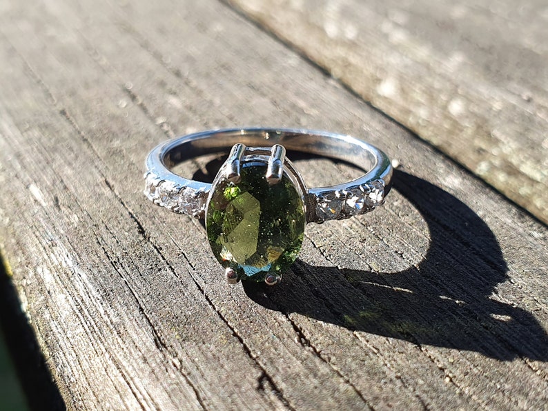 May include: A silver ring with a green oval gemstone and small clear stones set in the band.